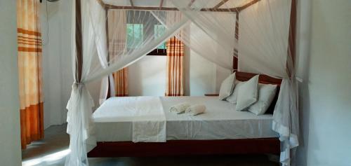 1 dormitorio con cama con dosel, sábanas y almohadas blancas en Twinkle Tangalle Villa en Tangalle