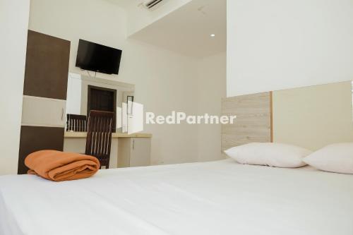 ein weißes Bett mit einer orangefarbenen Decke darüber in der Unterkunft Radja Homestay Mitra RedDoorz in Pipulu