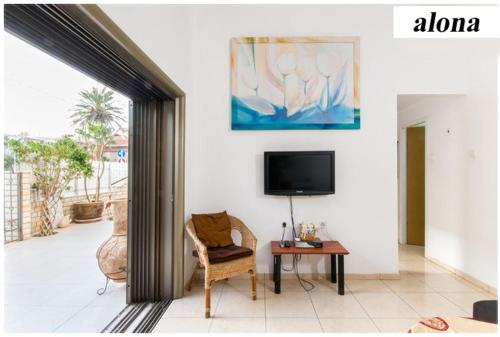 a living room with a tv and a chair and a table at Alona's Apartments - Beach Apartment in Haifa