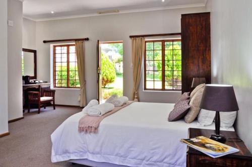 a bedroom with a large bed with a desk and windows at Thorntree Country Lodge in Oudtshoorn