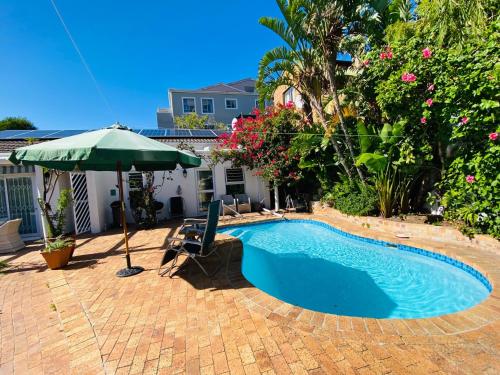 a swimming pool with a green umbrella and a chair and an umbrella at Sunbird in Hout Bay