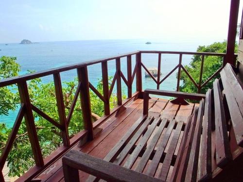 a bench sitting on a wooden balcony overlooking the ocean at OK2 Mamajim Bungalows in Koh Tao