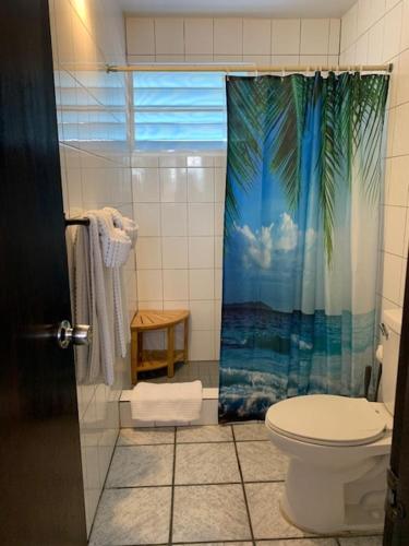 a bathroom with a toilet and a tropical shower curtain at Esperanza Inn Guesthouse in Vieques