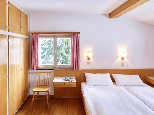 a bedroom with two beds and a chair and a window at Adele (704 De) in Lenzerheide