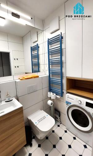 a bathroom with a toilet and a sink and a washing machine at Pod Brzozami Apartamenty Let's Sea Gąski in Gąski