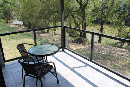 a balcony with a glass table and chairs on it at At the River Guest House in Kroonstad