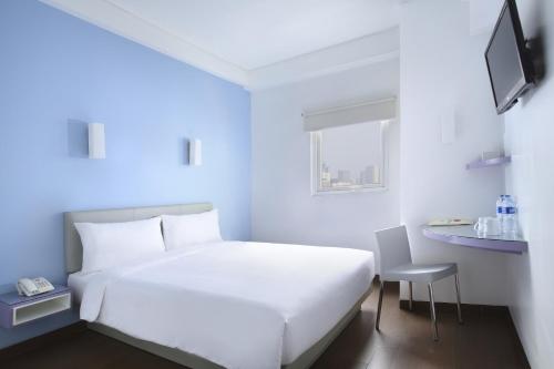 un letto bianco in una stanza con una sedia e una finestra di Amaris Hotel Bekasi Barat a Bekasi