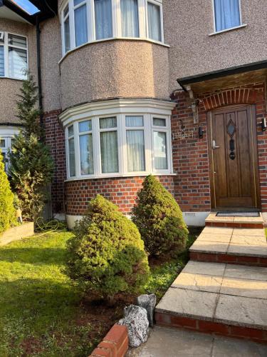 a brick house with a brown door and some bushes at TJ Homes - Luxury Studio Suite with Garden View - Next to tube station London in Ruislip