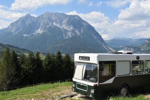 a bus parked in a field with mountains in the background at Glampingbus Lindwurm in Irdning