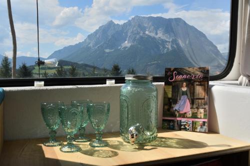 a table with glasses and a bottle on it with a mountain at Glampingbus Lindwurm in Irdning