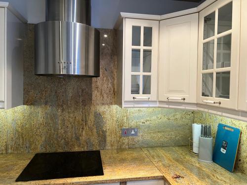 a kitchen with white cabinets and a stainless steel hood at TJ Homes - Luxury Studio Suite with Garden View - Next to tube station London in Ruislip