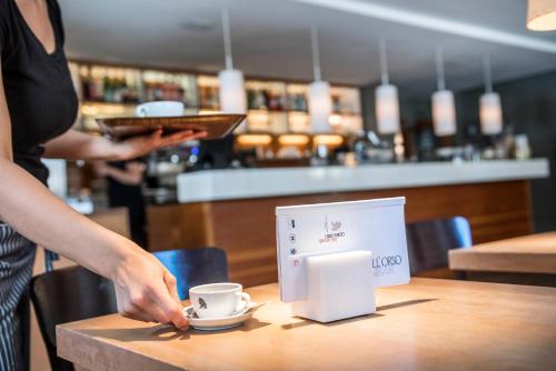 a woman standing at a table with a coffee cup on it at Boutique & Gourmet Hotel Orso Grigio in San Candido