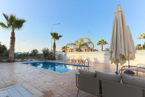 a pool with chairs and an umbrella and palm trees at Pernera Gardens Villa in Protaras