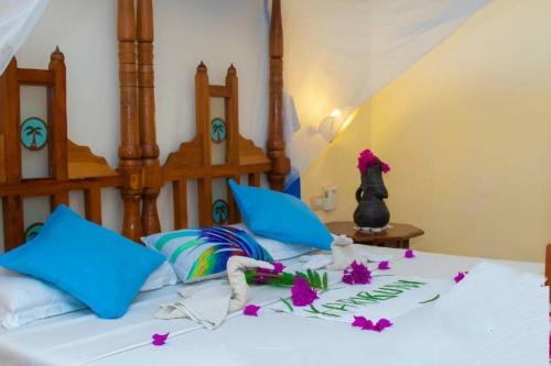 ein Bett mit blauen Kissen und lila Blumen darauf in der Unterkunft Tembo Beach Cottage in Malindi