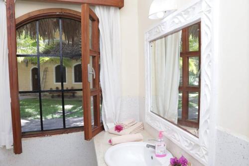 La salle de bains est pourvue d'un lavabo, d'un miroir et d'une fenêtre. dans l'établissement Tembo Beach Cottage, à Malindi