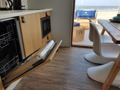 a living room with a dishwasher and a table with a view of the beach at Strandhuis, Beachhouse - Slapen op het strand, Sleep at the beach in Nieuwvliet