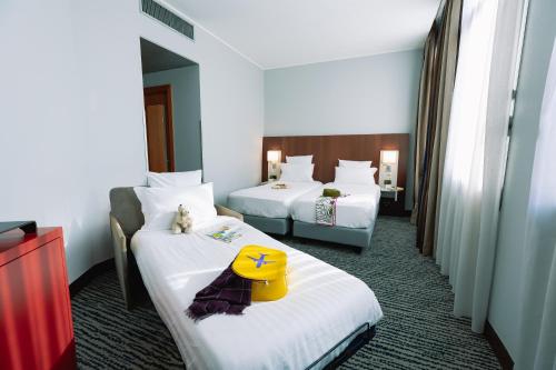 una camera d'albergo con due letti e un cappello giallo di Mercure Roma Piazza Bologna a Roma