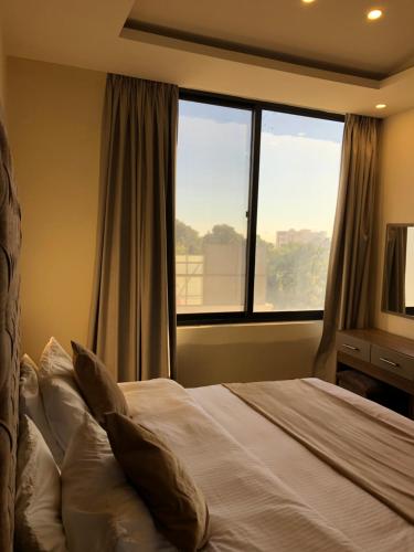 a bedroom with a bed and a large window at AlQimah Hotel Apartments in Amman
