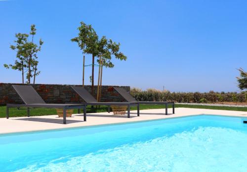 a swimming pool with two benches next to a brick wall at The Nine Graces - Kastraki Villas with Private Swimming Pool in Kastraki Naxou