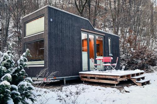a black tiny house in the snow with a table and chairs at Tiny House Nature 3 - Green Tiny Village Harz in Osterode