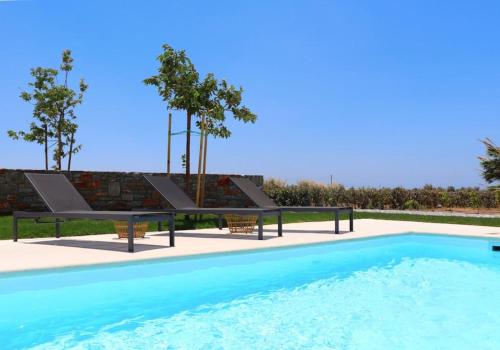 a swimming pool with two benches next to a brick wall at The Nine Graces - Kastraki Villas with Private Swimming Pool in Kastraki Naxou