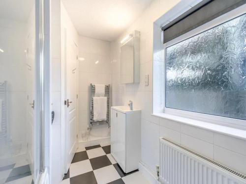 a white bathroom with a window and a checkered floor at Sandcastles - Mount Brioni in Downderry