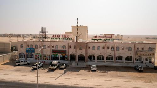 un gran edificio con coches estacionados frente a él en Arabian Sands Hotel فندق الرمال العربية, en Haymāʼ