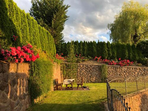 un giardino con panchina, fiori rossi e parete in pietra di Haus Ploner a Castelrotto