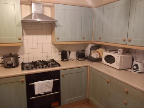 a kitchen with a stove and a microwave at Lovely Shared 3 Bed Home Near The Thames in Thamesmead