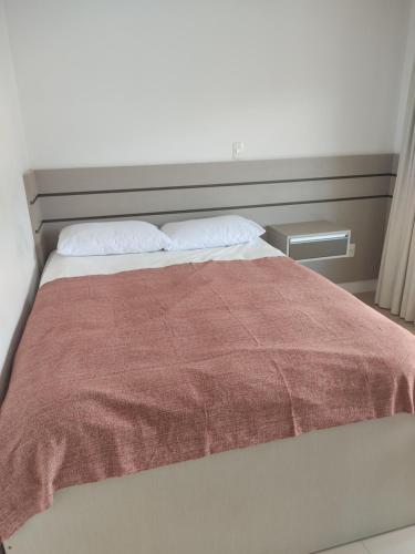1 cama con manta roja y 2 almohadas en Residencial Maristela, en Bombinhas