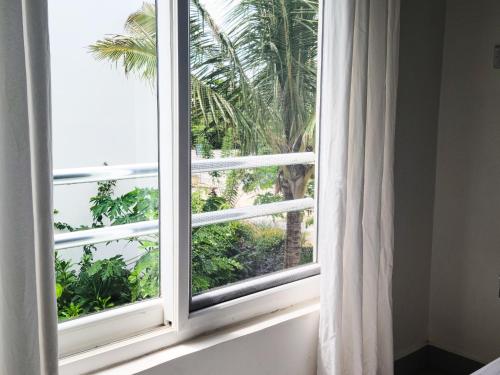 a window with a white curtain and a palm tree at Modern Apartment - Work from Zanzibar (Fumba Town) in Dambani