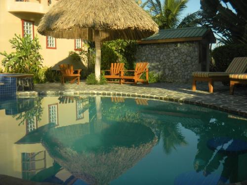 a swimming pool with chairs and a straw umbrella at Placencia Pointe Townhomes #5 in Placencia Village