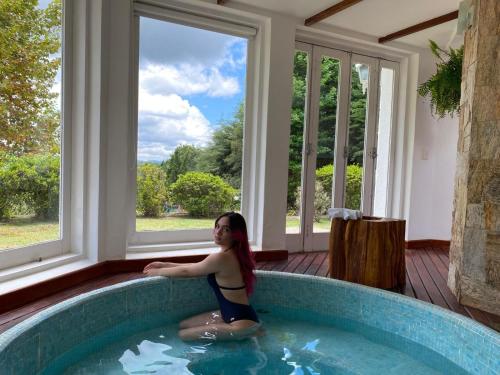 a woman sitting in a bath tub in a room with windows at Capivari Lodge vista incrível da natureza in Campos do Jordão