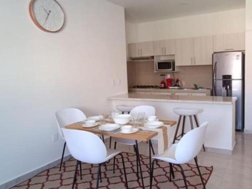 a kitchen with a wooden table and white chairs at Hermoso condominio con alberca en Puerto Morelos in Puerto Morelos
