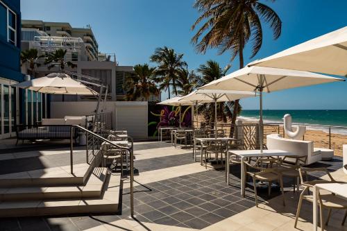 un patio con mesas y sombrillas y la playa en The Tryst Beachfront Hotel en San Juan