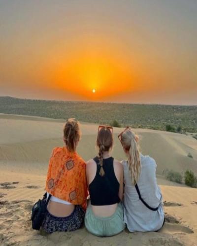 three women sitting in the sand watching the sunset at Naman Haveli-Boutique Stay For Budget Travllers in Jaisalmer