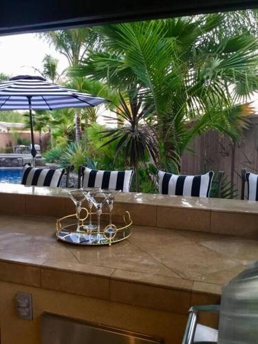 a table with a tray of wine glasses and an umbrella at Vino Villa Large home Sleeps 10! Large Salt water pool/spa in Murrieta