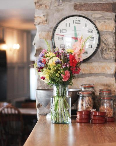 a vase of flowers on a table with a clock at The Five Dials Inn in Ilminster