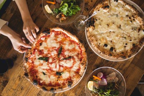 a wooden table topped with three pizzas and salad at TheMana Village in Tosashimizu