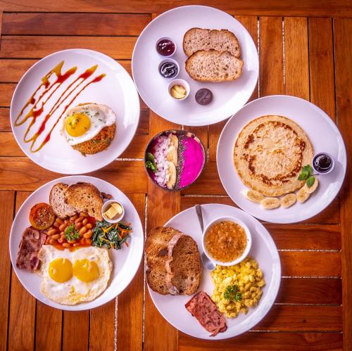 four plates of breakfast food on a wooden table at Mango Lodge in Selong Belanak