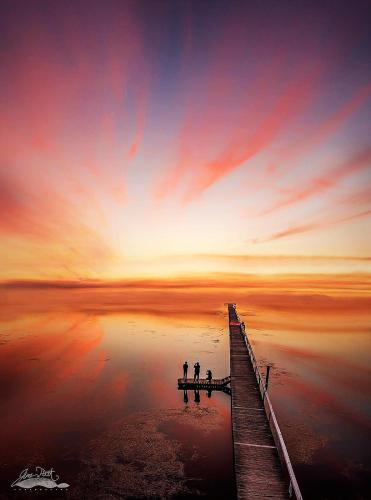 two people standing on a pier over the water at sunset at Jetty Motel The Entrance in The Entrance