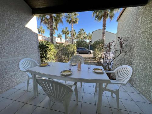 une table et des chaises blanches sur une terrasse avec des palmiers dans l'établissement Pavillon à Valras-Plage avec Piscine, Jardinet, Proche Plage et Commerces, Capacité 6 Personnes - FR-1-701-23, à Valras-Plage