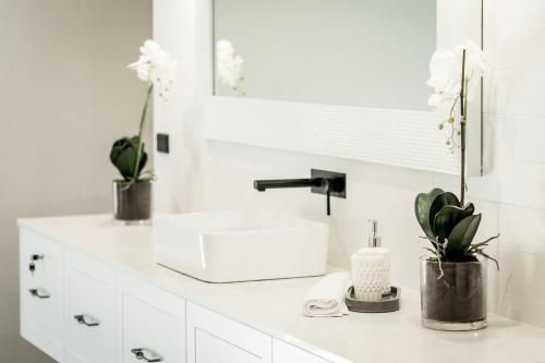 a white bathroom with a sink and flowers on a counter at Whitevale Luxury Estate in Lovedale