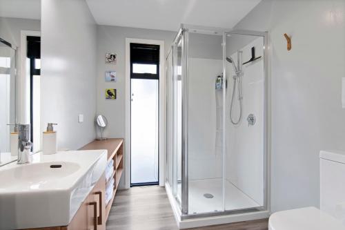 a white bathroom with a shower and a sink at Kotuku Apartment - Kaiteriteri Holiday Unit in Kaiteriteri