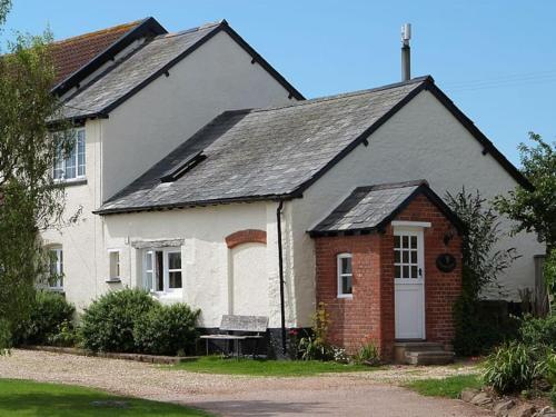 uma casa branca e vermelha com um banco à frente em Highdown Farm Holiday Cottages em Cullompton