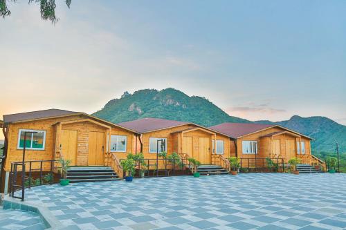 a row of wooden lodges with mountains in the background at Bamboo Saa Resort & Spa - Udaipur in Udaipur