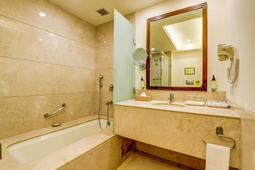 a bathroom with a tub and a sink and a mirror at Lemon Tree Hotel Electronics City in Bengaluru