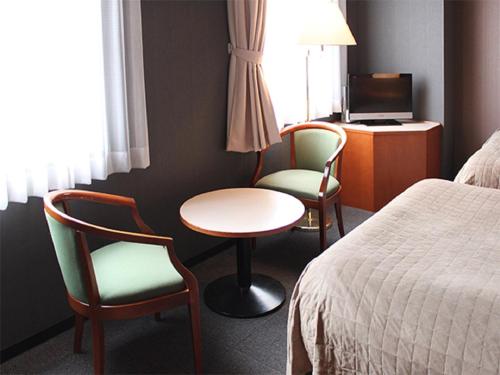 una camera d'albergo con due sedie, un tavolo e un letto di HOTEL LiVEMAX BUDGET Hiratsuka Ekimae a Hiratsuka