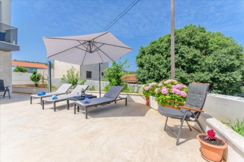 un patio con sillas, sombrilla y flores en Villa LA, en Veliki Drvenik