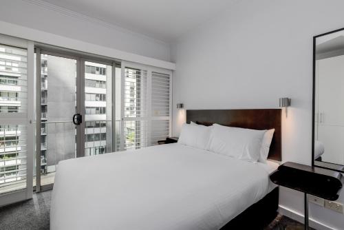a bedroom with a large white bed and large windows at Alto Hotel On Bourke in Melbourne